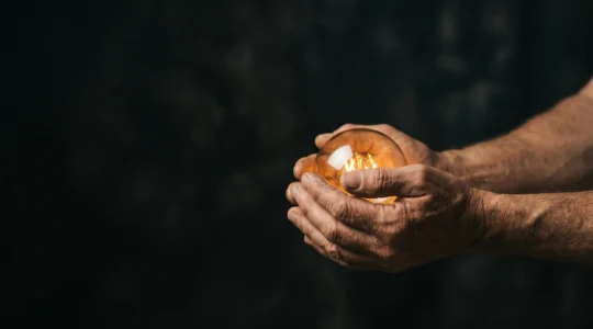 Deux mains tenant délicatement une lanterne lumineuse dans l'obscurité, symbolisant la transmission d'une histoire de marque authentique